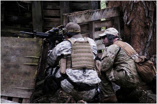 Airsoft-Spieler hinter einer Holzdeckung im Wald